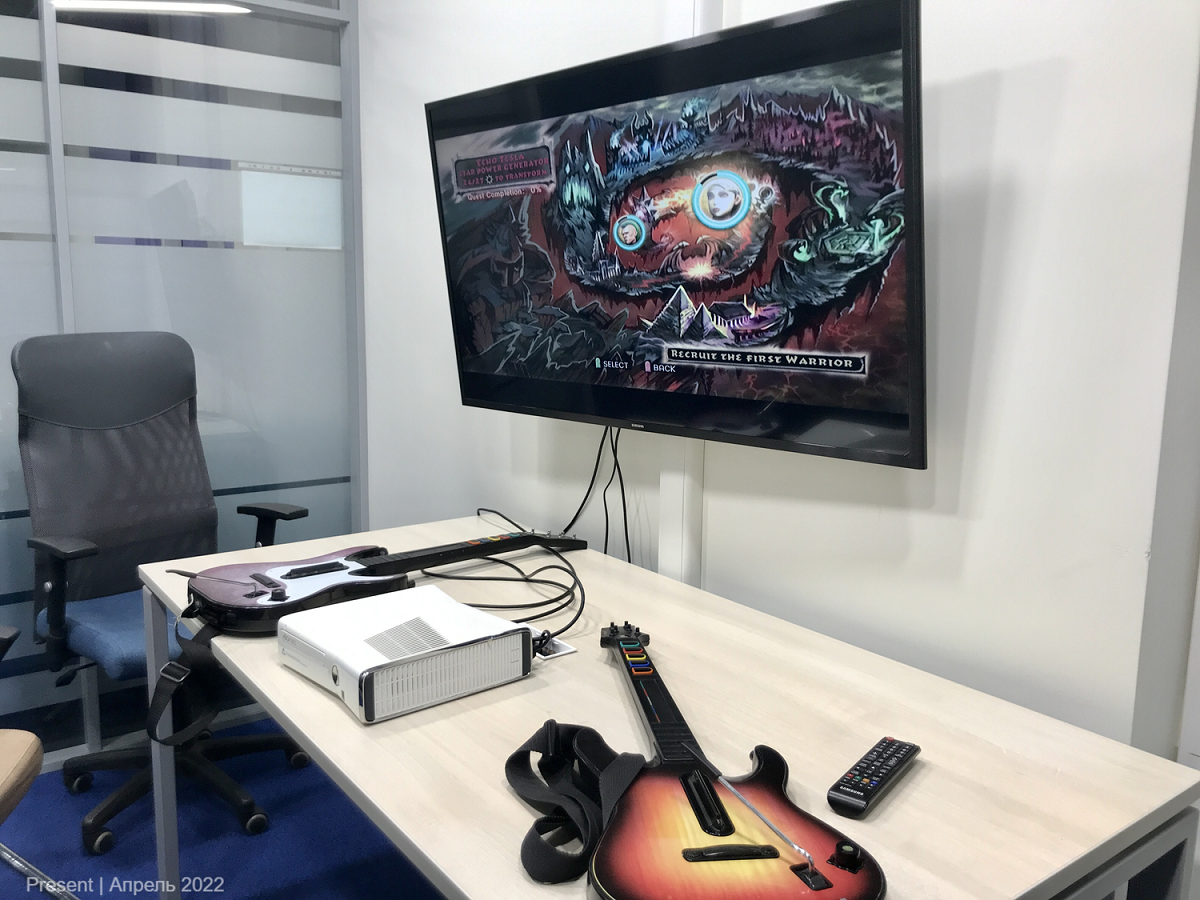 игра Guitar Hero на столе с гитарой, Xbox и экраном, показывающим игру.