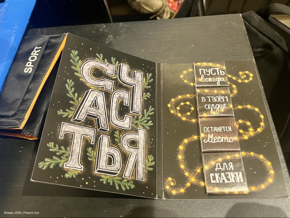 Открытая открытка с надписью 'СЧАСТЬЕ' и декоративными элементами, на страницах которой написаны пожелания, окружённые огоньками.