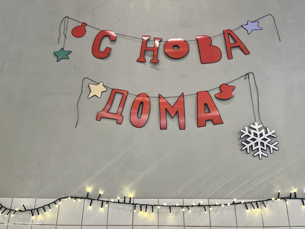 Надпись "С Новым Домом" с новогодними украшениями на стене.
