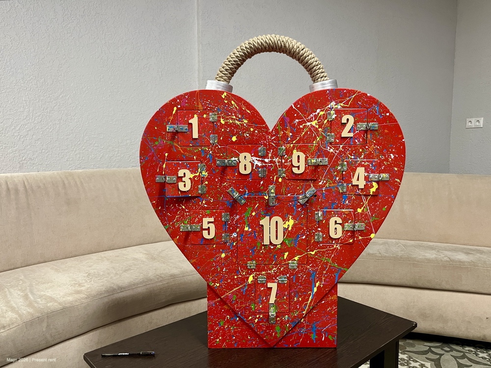 Креативный адвент-календарь в форме сердца, окрашенный яркими цветами и с номерками от 1 до 10. Расположен на столе в уютной комнате.