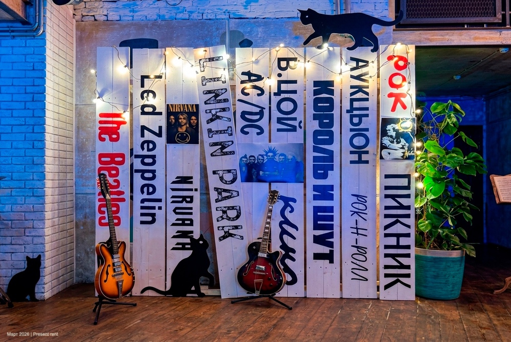 Задник для музыкантов с названиями рок-групп и светящимися огоньками, две гитары и украшения в виде черных кошек.