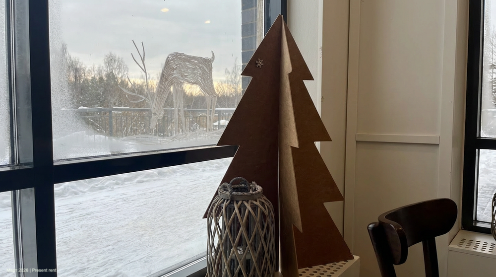Новогодняя композиция с картонной елкой и стеклянной вазой у окна, за которым виден снежный пейзаж и силуэт оленя.